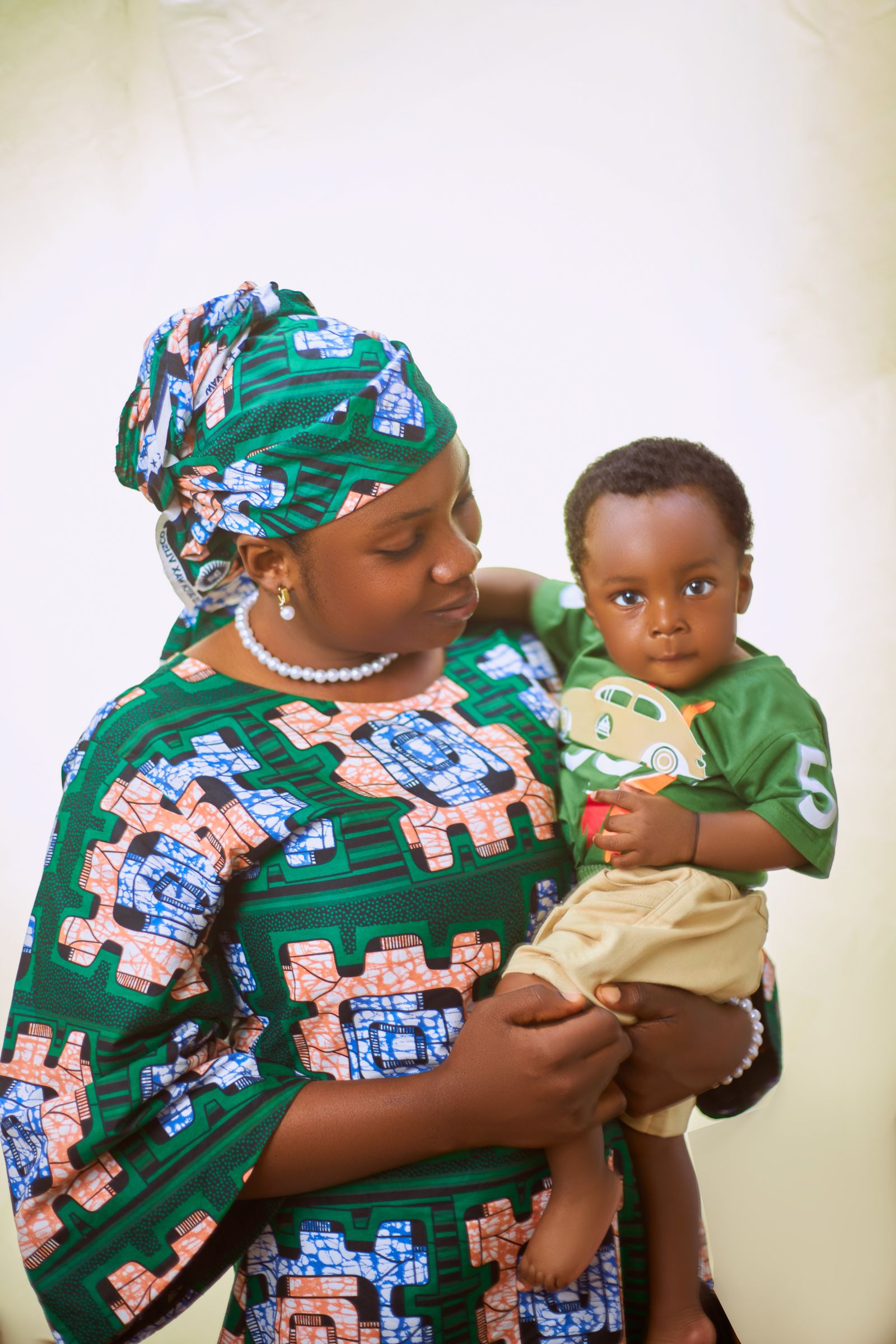A mother in a green patterned dress and headwrap holds her young son.