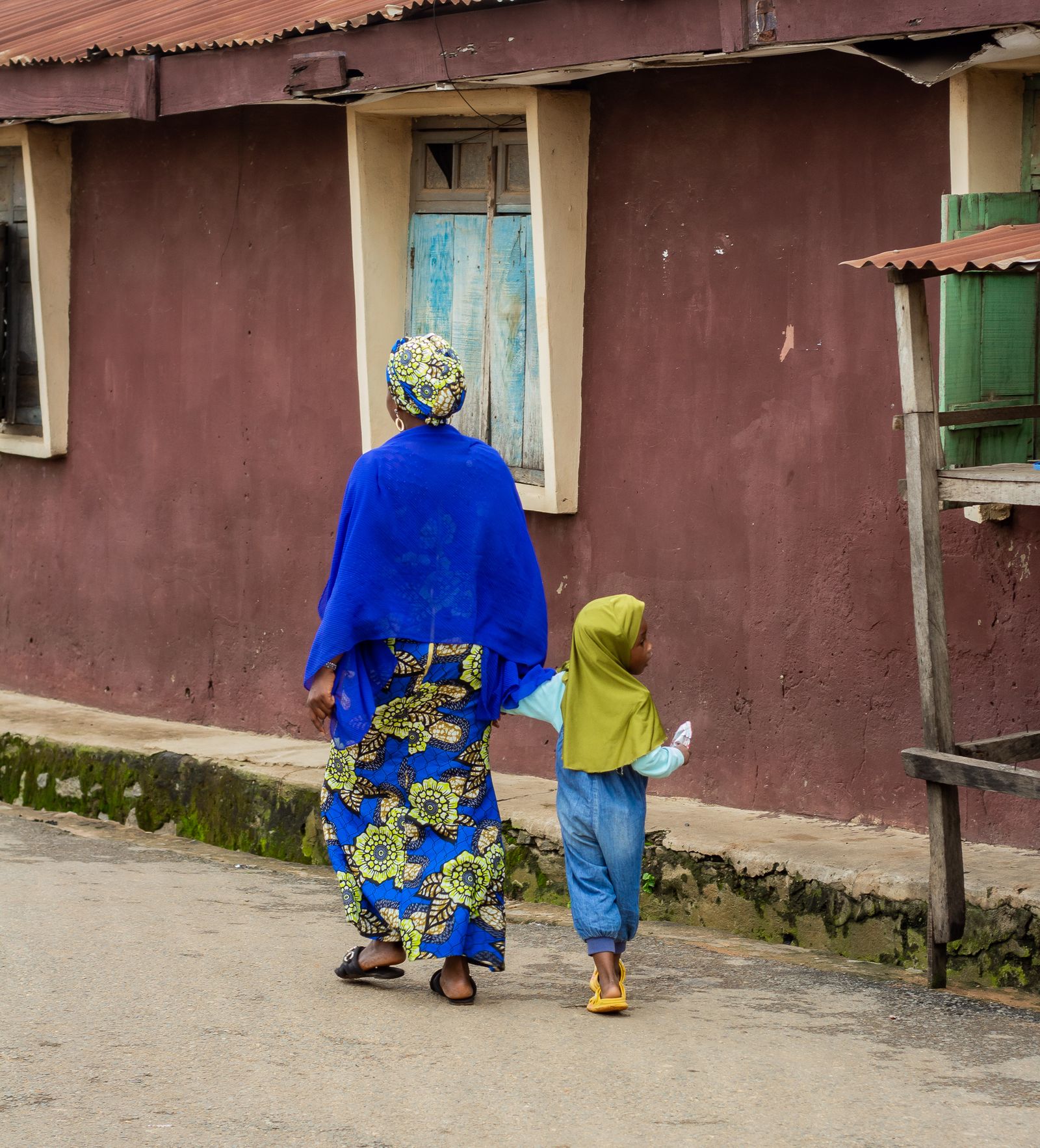A mother in a blue wrapper walks hand in hand with her small child.