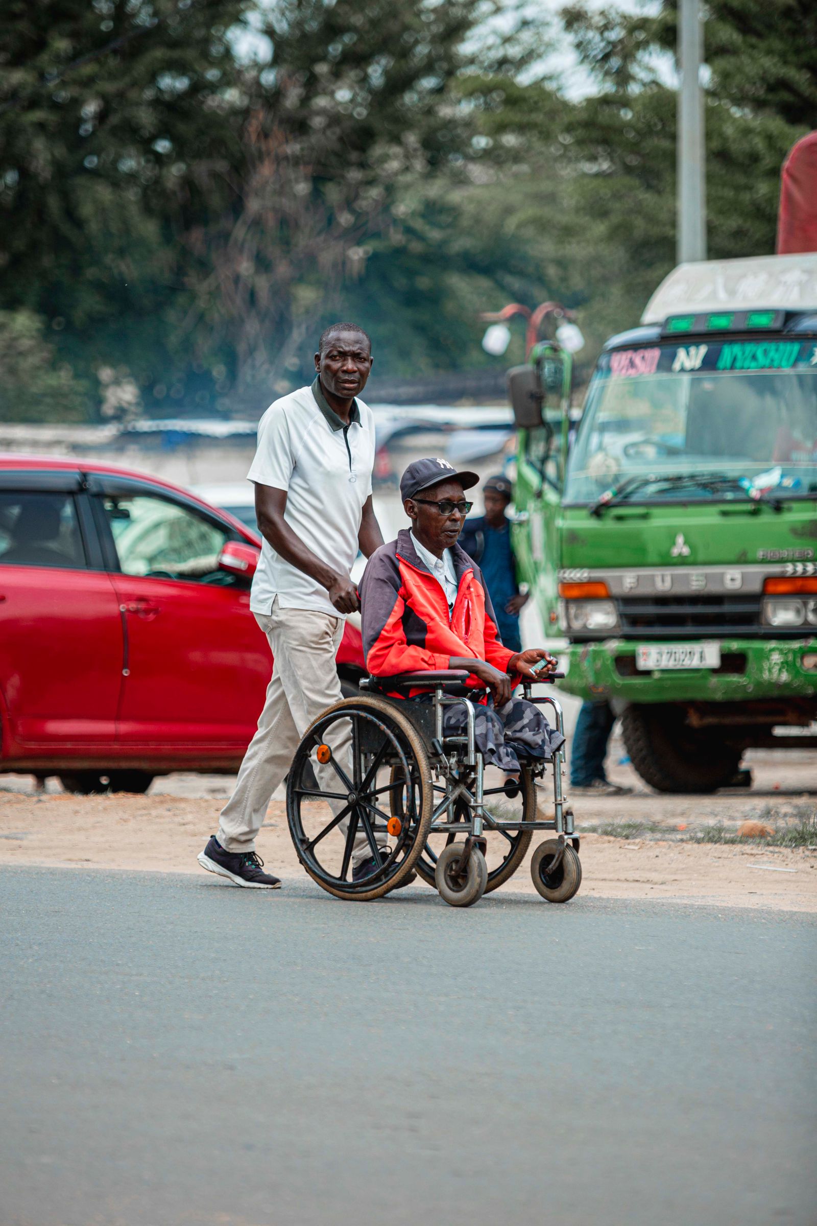 A father pushes his son in a wheelchair along a city road.